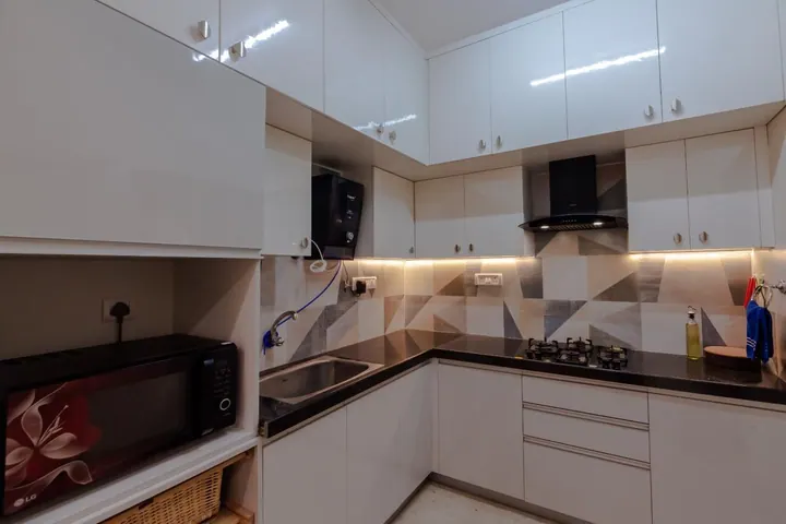 L-shaped modular kitchen with white gloss shutters and a geometric tile backsplash